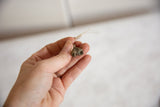 A hand holding the small vintage African bronze bell pendant to show its scale and texture.