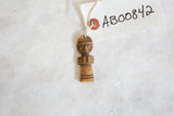 A vintage African wooden pendant with carved geometric patterns on its face and body.