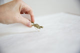 A hand holding the small bronze turtle pendant to illustrate its scale and mesh texture.