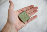 Oxidized bronze African coin with textured green patina held in palm.