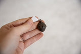 Vintage dark bronze mask pendant held in hand to show its small scale.