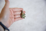 Vintage African bronze mask pendant held in hand to illustrate its scale and texture.