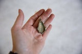 Reverse side of the oxidized bronze mask pendant showing its hollow, handcrafted form.