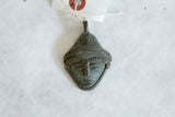 Stylized face of a vintage African bronze pendant with a dark, time-softened patina.