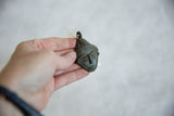 Vintage African bronze mask pendant held in hand to show its scale and texture.