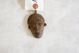 The textured surface and hand-carved details of a vintage African bronze mask pendant.