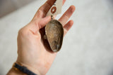 Reverse side of the vintage bronze mask pendant showing its hollow interior and handmade texture.