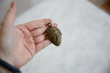 Vintage African bronze mask pendant held in hand to show its scale and handmade detail.