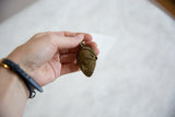 Vintage African bronze mask pendant held in hand to show scale.