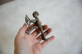 Vintage African aluminum archer held in hand, showing textured surface and tabletop mounting base.