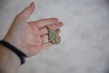 Vintage bronze hut pendant with bug design shown in hand for scale.