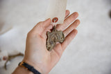 Vintage African bronze pendant held in hand to demonstrate its scale and rustic texture.
