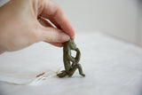 Hand holding a small vintage African oxidized bronze monkey sculpture with green patina.