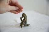 Vintage oxidized bronze monkey sculpture, weathered green patina, and human hand.