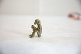 Side profile of vintage African oxidized bronze monkey sculpture, hands clasped around a banana.