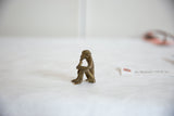 Full profile of a vintage bronze sitting monkey sculpture eating a banana.