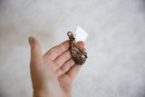 Vintage African bronze instrument pendant held in hand to show its scale and unique form.