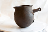 Antique African wooden pitcher with hand-carved details and a metal repair patch.