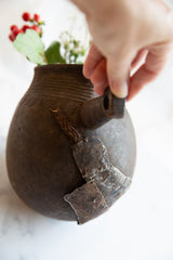 Hand holding the spout of an antique wooden pitcher with rustic metal repairs.