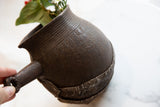 Hand holding the antique African wooden pitcher, showing its carved neck and rustic finish.