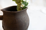The rustic character and carved details on the neck of an antique wooden pitcher.