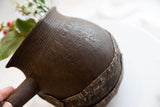 Hand-carved geometric patterns and aged metal repair on a rustic wooden pitcher.