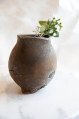 Angled view of an antique wooden pitcher displaying its dark rustic patina and cracks.