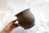 Profile of an antique wooden pitcher held in hand, showing its central repair.