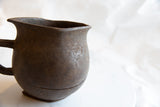 Angled view of the hand-carved spout and rim on a dark wooden pitcher.