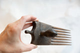 Hand holding antique handmade African wooden bird comb, revealing carved dark wood.