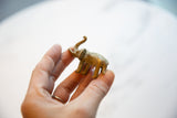 Hand holding a vintage African oxidized bronze elephant with trunk up and golden patina.