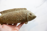 Vintage African bronze fish with detailed scales and greenish patina, held in a hand.