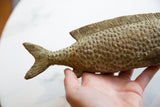 Bronze fish held in hand, displaying handmade texture and green patina.