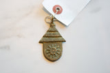 The textured, oxidized surface of the bronze hut-shaped pendant with sun motif.
