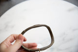 Hand holding antique African bronze artifact, revealing its curved shape and aged patina.
