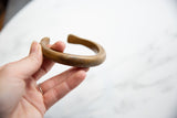 Antique bronze cuff held to show its substantial form and time-worn surface patina.