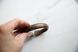 A hand holding the antique bronze cuff bracelet to show its smooth, time-worn patina.