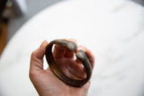 Hand holding the antique snake cuff, showing its curved form and aged surface.