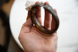 The handmade form and textured bronze patina of an antique snake cuff held in hand.