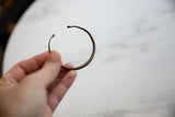 The slender, open-cuff shape of an antique African bronze bracelet with snakeskin texture.