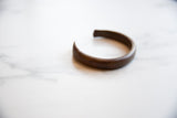 Side profile of the antique copper cuff bracelet, showing its curved form and dark, aged patina.