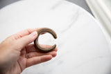 The aged patina and etched details on an antique bronze snake cuff held in hand.