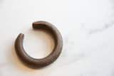 The open C-shape and rounded ends of the antique copper cuff with a dark, textured patina.