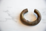 The thick, curved form and oxidized finish of a collectible antique African bracelet.