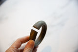 A hand holding an antique bronze cuff bracelet to show its thick, substantial open ends.
