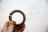 Hand holding the thick, C-shaped antique African bronze currency bracelet.