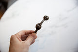 A hand holding the vintage Lobi bell cuff bracelet, showing its dark bronze patina.