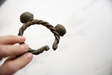 Hand-held view of the twisted bronze Lobi cuff showing its handcrafted form and bell ends.