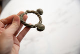 A hand holds the twisted bronze Lobi cuff, showing its aged patina and form.