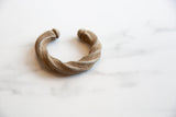 Angled profile of an antique twisted aluminum cuff with an aged patina.